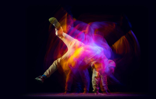 Solo dance. Young flexible sportive man dancing hip-hop or breakdance in white outfit on dark background in mixed yellow neon light. Beauty, sport, youth, action, moves - Foto, immagini