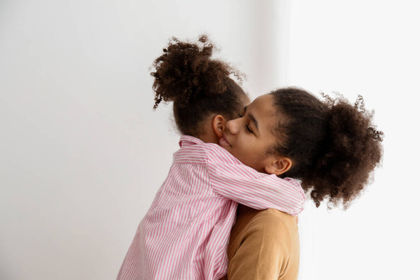 Younger and older sister spending time together at home. Two black girls of different age hugging and showing affection. Black female siblings having fun and bonding. Background, copy space, close up. - Foto, imagen