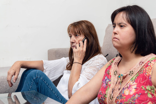 madre latina latina hispana caucásica sentada en el piso de la sala de estar hablando por teléfono mientras su hija mira televisión, familia y concepto de tecnología. - Foto, Imagen
