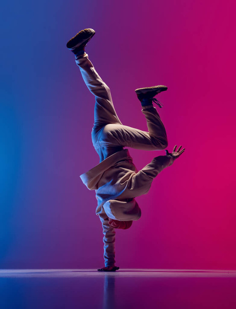 Studio shot of young flexible sportive man dancing breakdance in white outfit on gradient pink blue background. Concept of action, art, beauty, sport, youth - Photo, image