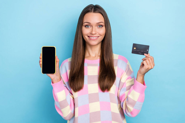 Photo of shopaholic lady hold phone screen empty space debit card wear pullover isolated blue color background - Foto, afbeelding