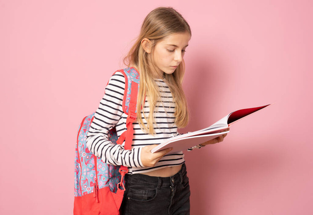 Mladá krásná dívka na sobě student batoh čtení knihy stojí izolované nad růžovým pozadím. Koncept vzdělávání. - Fotografie, Obrázek