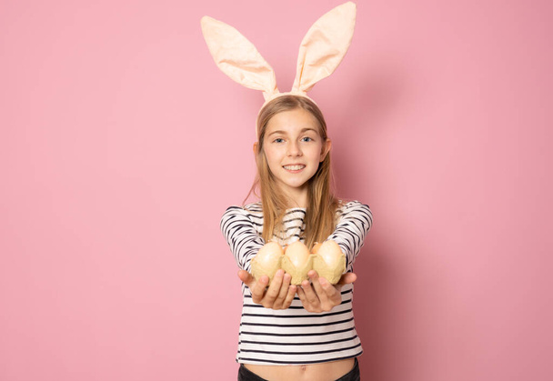 Зі святом Великодня. Красива молода дівчина посміхається в кролячих вухах, тримаючи великодні яйця на руці ізольовані на рожевому фоні
. - Фото, зображення