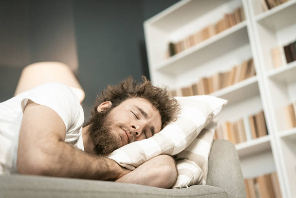 Sleeping on the sofa handsome bearded young man hugging a pillow after a long hours working late nigh. Sick young man sleeping on the couch after taking medications. distance work concept - Foto, Imagem