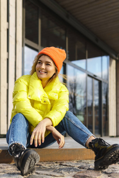 Portrait of  stylish girl wearing yellow puffer and orange knitted hat  - Фото, изображение