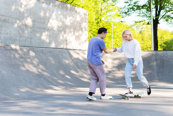 Dating or friendship. Carefree teenage couple in a skate-park. Guy giving a lesson of skateboarding for his girlfriend.  - Foto, imagen