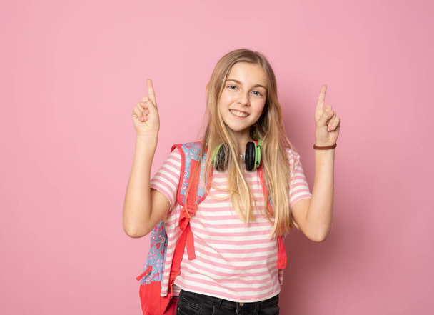 Νεαρό όμορφο κορίτσι φοράει φοιτητικό σακίδιο δείχνοντας τα δάχτυλα ψηλά στέκεται απομονωμένο πάνω από ροζ φόντο. Εκπαιδευτική έννοια. - Φωτογραφία, εικόνα