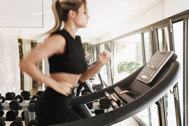 Young athletic woman running on treadmill during fitness workout. Long exposure for motion blur. - Photo, Image