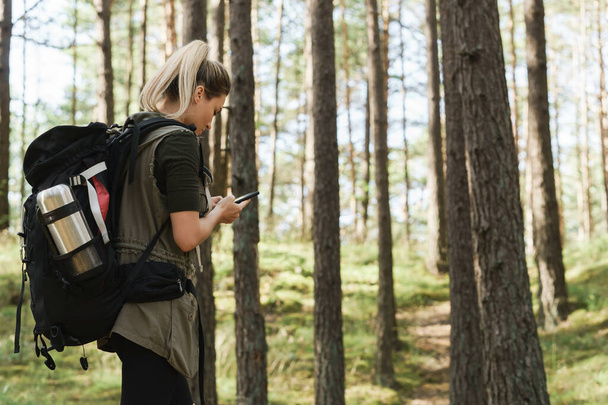 Young female hiker is using smartphone for navigation in green forest - Foto, Imagen