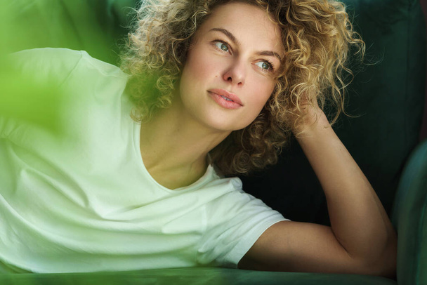 Portrait of young and beautiful woman with curly hair lying on green sofa - Foto, imagen