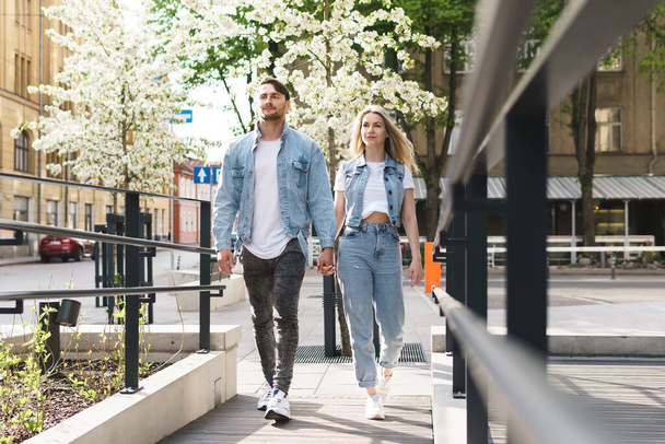 Portrait of young confident and loving couple wearing denim outfits walking during their date on a city street - Фото, изображение