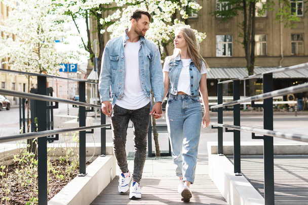 Portrait of young confident and loving couple wearing denim outfits walking during their date on a city street - Foto, Imagem