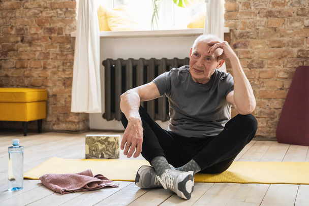 Активний літній чоловік розслабляється після тренування фітнесу вдома
 - Фото, зображення