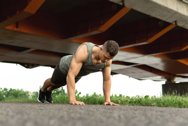 Young and muscular man is doing push-ups during calisthenic workout on a street - Fotó, kép
