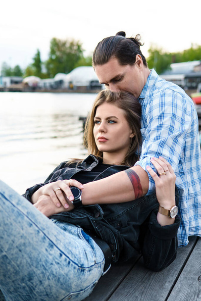 Portrait of young sensual and loving couple sitting on a pier beside a river - Photo, image
