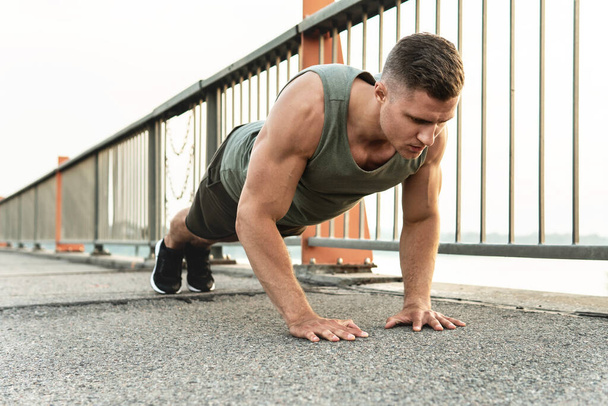 Young and muscular man is doing push-ups during calisthenic workout on a street - Zdjęcie, obraz
