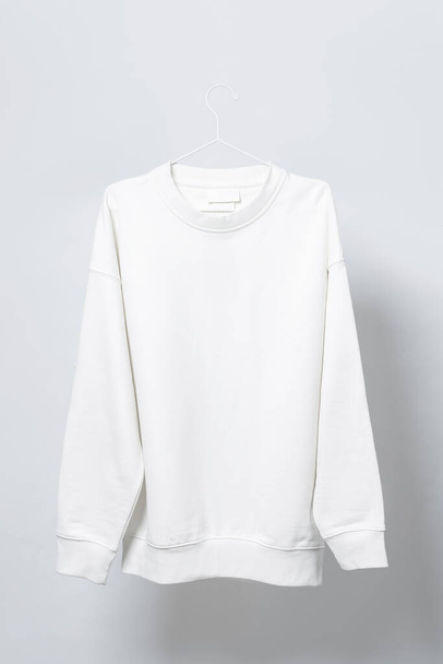 Blank white sweatshirt hanging on the thin metallic hanger against light gray background - Фото, изображение
