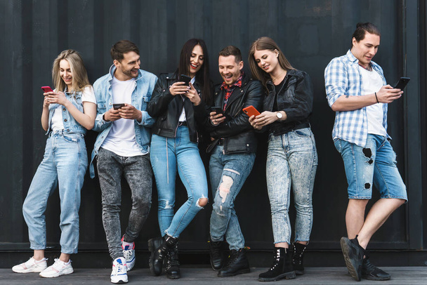 Group of young and stylish friends using smartphones for messaging instead of real communication - 写真・画像