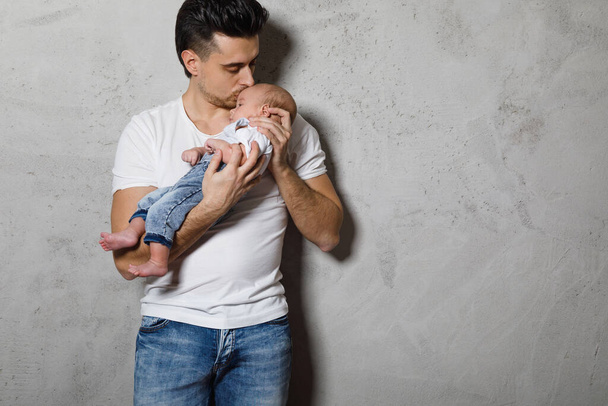 Young loving father holding his cute little baby boy against concrete wall - 写真・画像