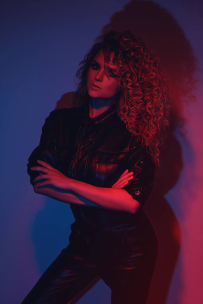 Young and sexy woman with a stylish Afro hairstyle wearing leather biker suit posing in colorful neon light - Fotoğraf, Görsel