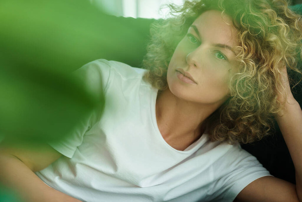 Portrait of young and beautiful woman with curly hair lying on green sofa - Фото, зображення