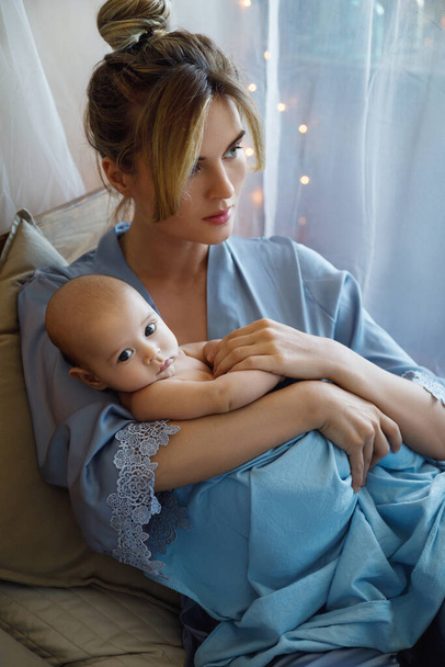 Portrait of young beautiful mother with her cute little baby wrapped in the blue cloth - Valokuva, kuva