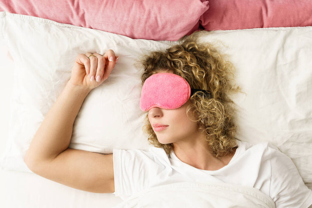 Beautiful woman sleeping with a pink blindfold on her eyes in the bed - Φωτογραφία, εικόνα