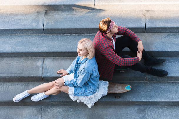 Top view of stylish teenage couple with a longboard is sitting on a concrete stairs - Foto, Imagem