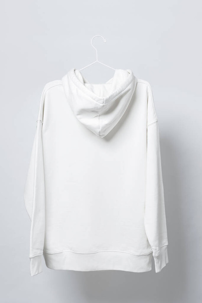 Blank white hoodie hanging on the thin metallic hanger against light gray background - Foto, imagen