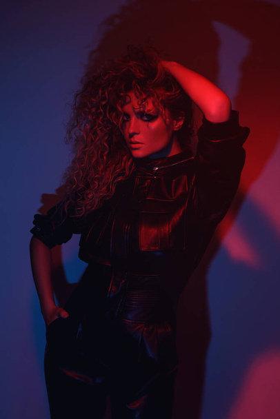 Young and sexy woman with a stylish Afro hairstyle wearing leather biker suit posing in colorful neon light - Φωτογραφία, εικόνα