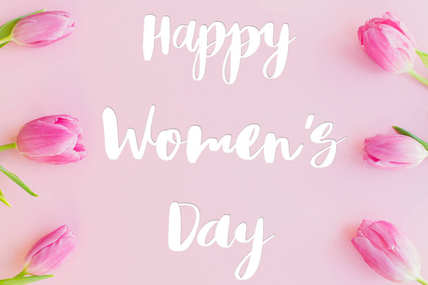 Happy womens dagtekst op roze tulpen plat lag op roze achtergrond. Stijlvolle wenskaart. Internationale Vrouwendag. 8 maart. Handgeschreven belettering - Foto, afbeelding