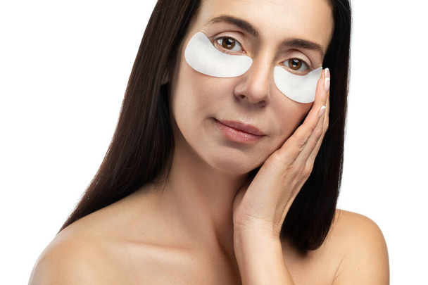 Anti aging treatment. Middle aged woman with applied sheet patches under her eyes on white background. - Фото, зображення