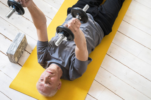 Active elderly man exercising with a dumbbells during his workout in home gym - Photo, image