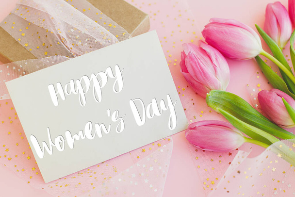Счастливого женского дня текст на поздравительной открытке, розовые тюльпаны и подарочная коробка на розовом фоне. Стильная поздравительная открытка. Международный женский день. 8 марта. Письменное письмо - Фото, изображение