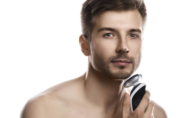 Young and handsome man is using modern electric shaver on white background - Фото, зображення