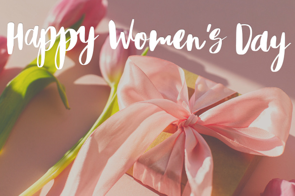 Texto de feliz día de las mujeres en tulipanes rosados y caja de regalo a la luz del sol sobre fondo rosa. Tarjeta de felicitación con estilo. Día Internacional de la Mujer. 8 de marzo. Letras manuscritas - Foto, imagen