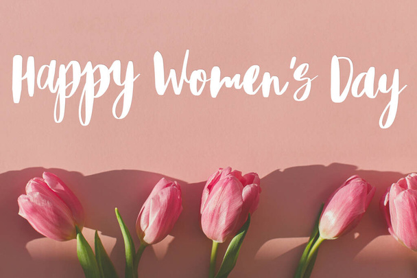 Texto feliz día de las mujeres en tulipanes rosados en la luz del sol sobre fondo rosa plana laico. Tarjeta de felicitación con estilo. Día Internacional de la Mujer. 8 de marzo. Letras manuscritas - Foto, imagen