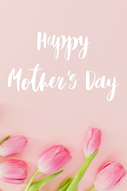 ピンクのチューリップの幸せな母の日のテキストはピンクの背景に平らなレイアウト。スタイリッシュなグリーティングカード。母の日、感謝と母への愛。手書き文字 - 写真・画像