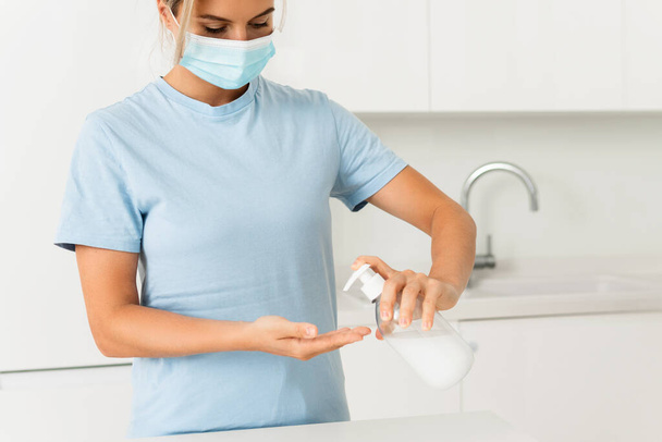 Nainen yllään ennaltaehkäisy naamio käyttää käsi puhdistusaine tai nestemäinen saippua käsien desinfiointiin kotona - Valokuva, kuva