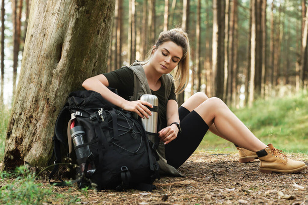 Young female hiker during small halt sitting in green forest - Foto, Bild