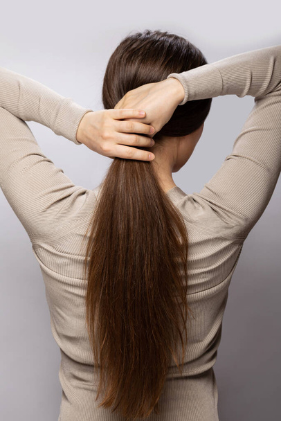 Mujer joven mostrando su cabello castaño sano natural sobre fondo gris - Foto, imagen