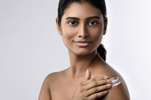 Mulher indiana bonita e feliz aplicando creme hidratante ou protetor solar loção em seu corpo
 - Foto, Imagem