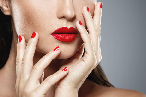Beauty and cosmetics. Close-up of female mouth and nails with red manicure and lipstick. - Valokuva, kuva