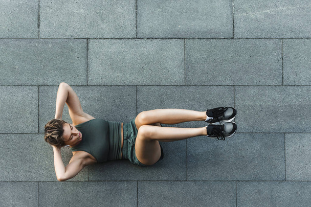 Young athletic woman doing abdominal crunches exercise on concrete floor during her street workout - Photo, Image