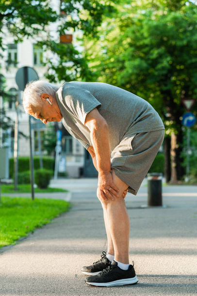 Starszy mężczyzna cierpiący na ból kolana podczas treningu joggingowego w parku miejskim - Zdjęcie, obraz
