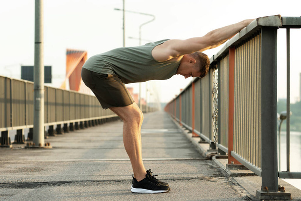 Fiatal atlétikai férfi bemelegszik, mielőtt az utcai edzés a hídon - Fotó, kép