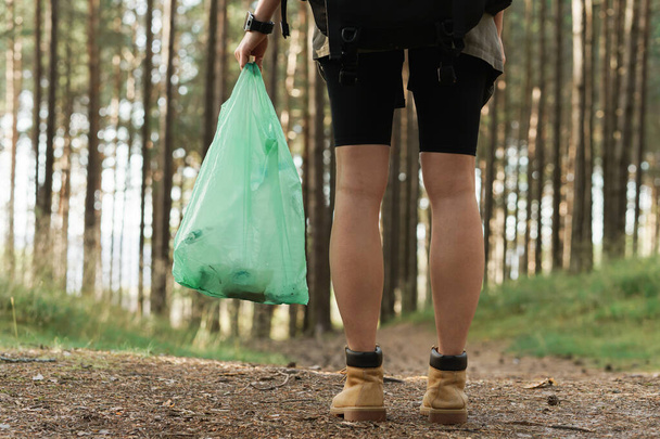 Young female hiker collecting plastic waste in green forest - Valokuva, kuva