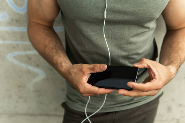 Athletic man holding black smartphone during his workout - Foto, imagen