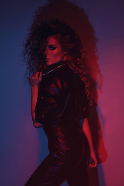 Young and sexy woman with a stylish Afro hairstyle wearing leather biker suit posing in colorful neon light - Foto, Bild