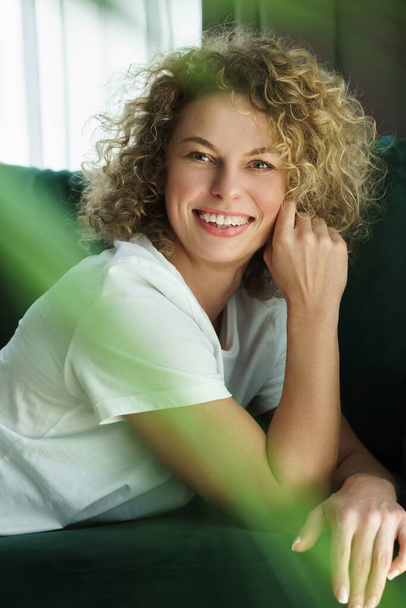 Portrait of young and beautiful woman with curly hair lying on green sofa - Foto, immagini